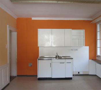 Eine alte, sehr einfache Küchen-Einbauzeile prägt hier das Bild vor kräftiger orangener Wand.